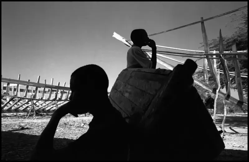 Two workers take a break from boat building in the shade. On the L'Ile de la Tortue boats are made by hand from pine trees, scrap wood and used nails and are then used in attempts to sail from Haiti to America carrying human cargo. This is the starting point for an epic voyage that many hope will take them to America. Haiti. 2000 © Christopher Anderson, Альбом: Christopher Anderson, Haiti. Immigrants Trip to America.